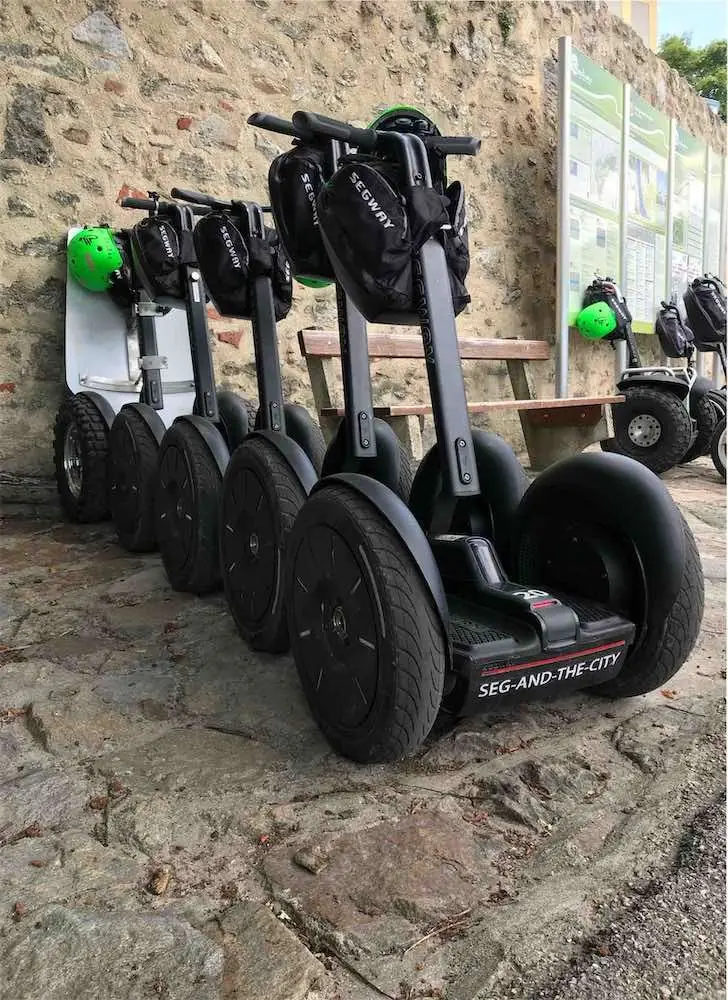 Segways in einer Reihe an einer Steinmauer, grüne Helme an den Lenkern