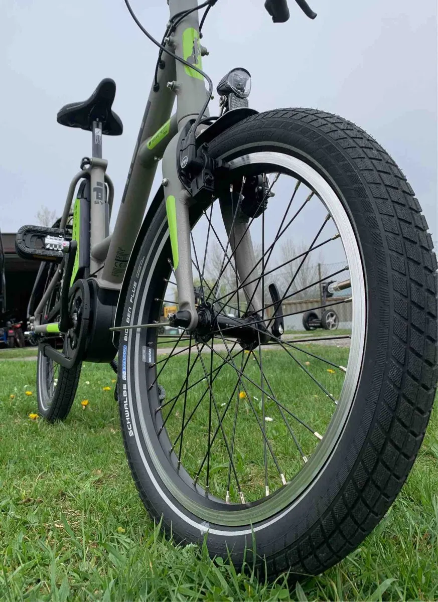 Graues i:SY E-Bike mit grünen Akzenten auf der Wiese, von unten am Vorderrad