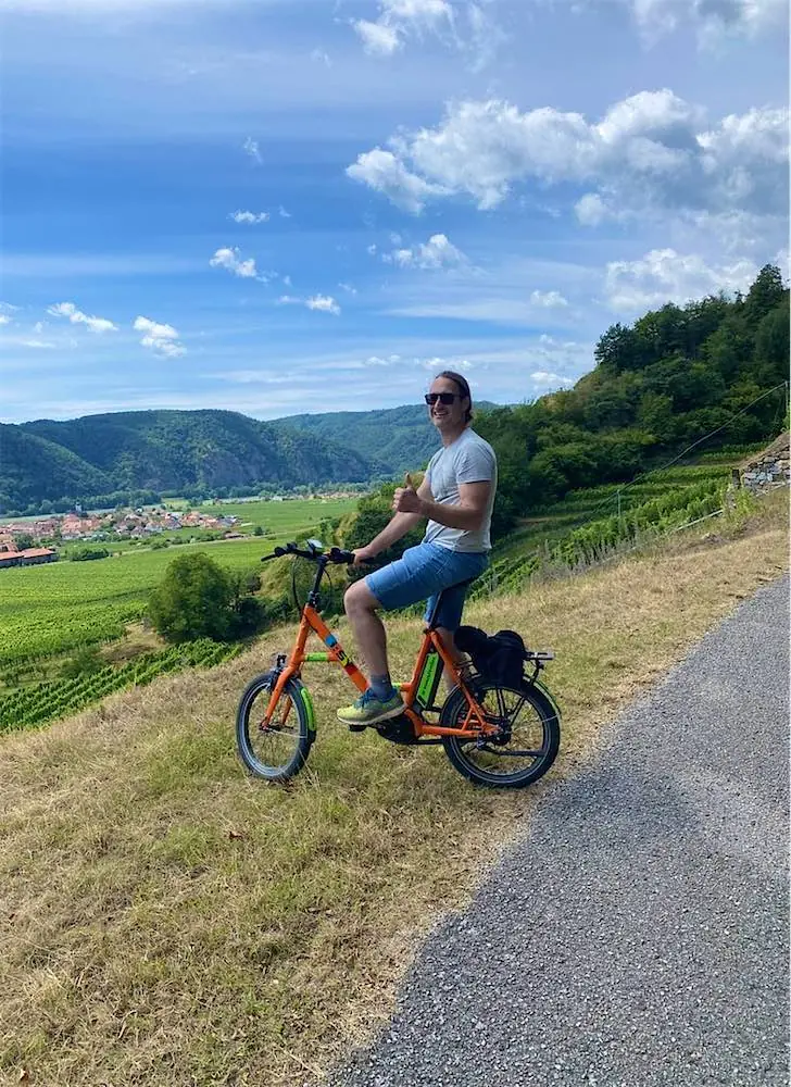 Radfahrer auf einem orangefarbenen E-Bike am Wegrand über den Weingärten der Wachau