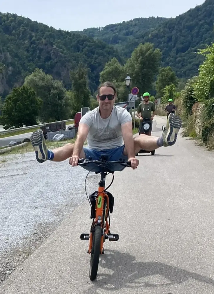 Radfahrer streckt auf dem E-Bike die Beine zur Seite, dahinter zwei Segway-Fahrer mit grünen Helmen