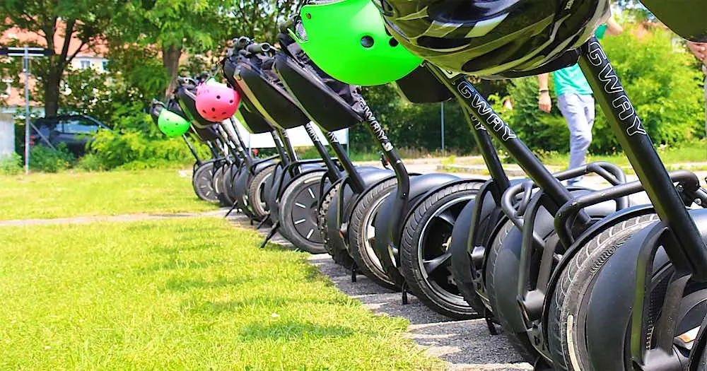 Segways in einer Reihe auf der Wiese, an den Lenkern hängen Helme
