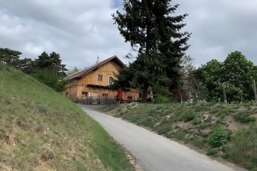Holzhaus mit Gastgarten an einem Weg zwischen Wiesenhängen und Bäumen