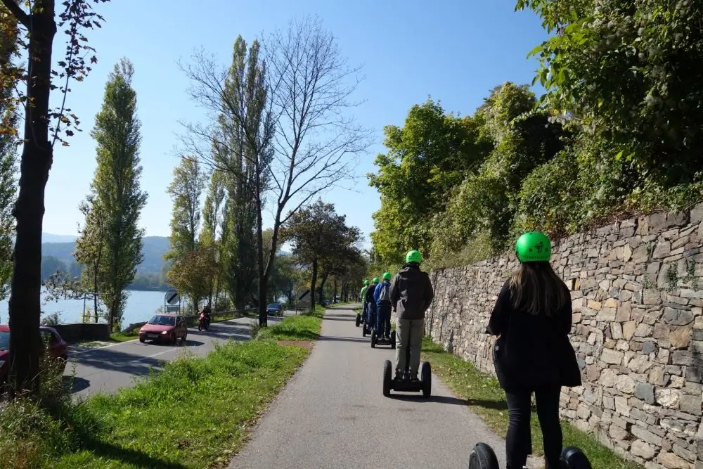 Segway-Gruppe mit grünen Helmen auf dem Radweg an einer Steinmauer, links die Donau
