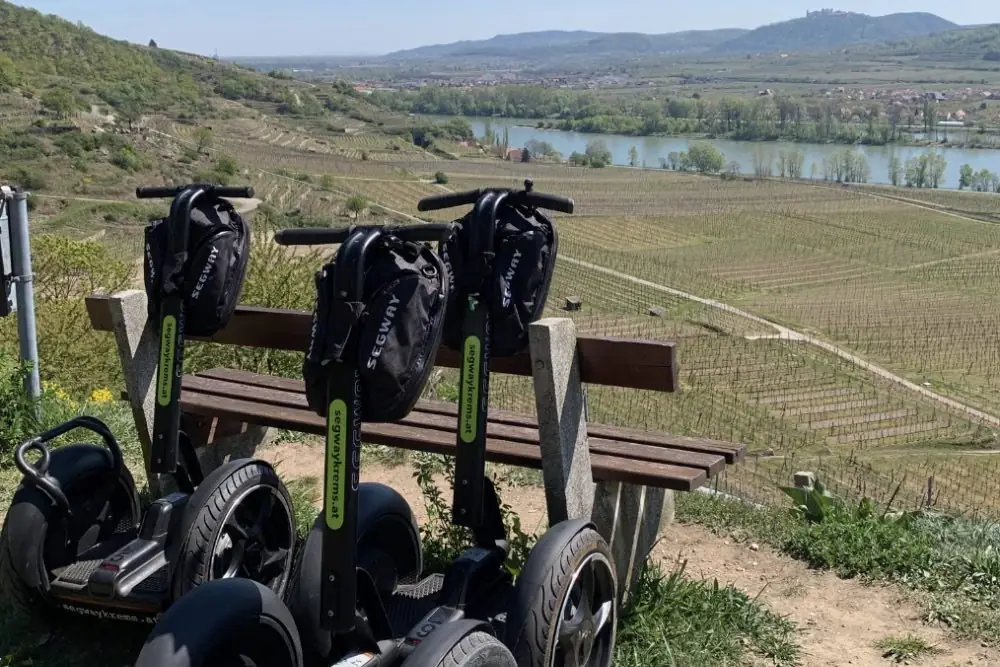 Drei Segways an einer Bank mit Blick über die Weingärten auf die Donau