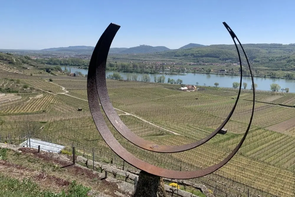 Bogenförmige Stahlskulptur über den Weingärten, dahinter die Donau